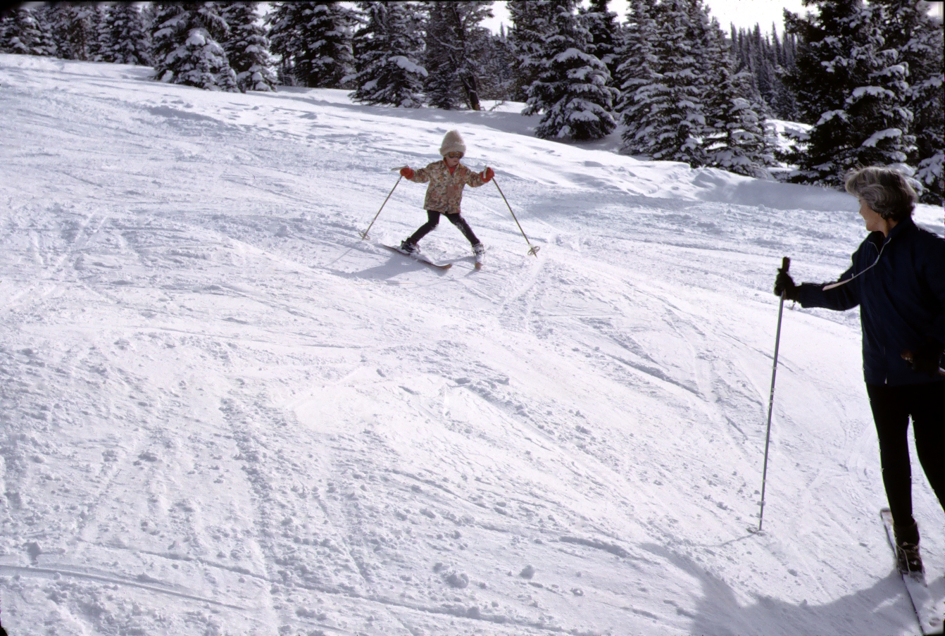 Vintage photo of a little girl skiing down a mountain while her mother looks on.